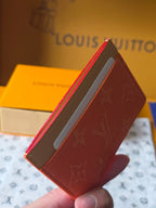 Small Louis Vuitton cardholder with coral orange exterior and beige interior panel, front edge.
