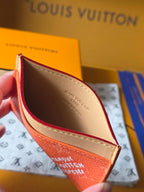 Small Louis Vuitton cardholder open view showing beige interior with coral orange outer pocket.