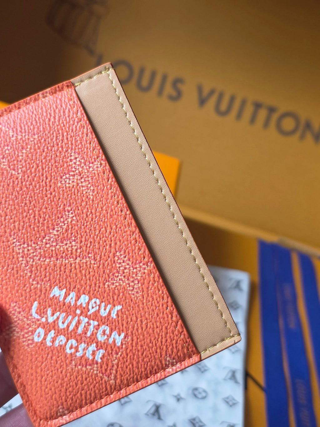 Small Louis Vuitton cardholder side view in coral orange with beige leather trim and logo text.