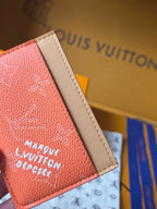 Small Louis Vuitton cardholder side view in coral orange with beige leather trim and logo text.