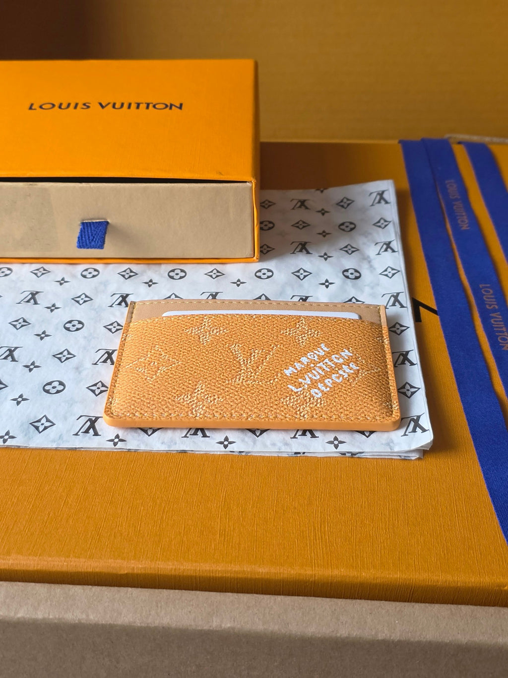 Louis Vuitton monogram card holder in tan leather with card slot, laid on patterned box