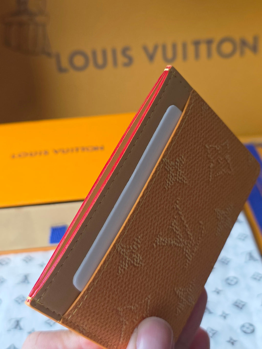 Small tan Louis Vuitton monogram bag side view with red trim and white card slot
