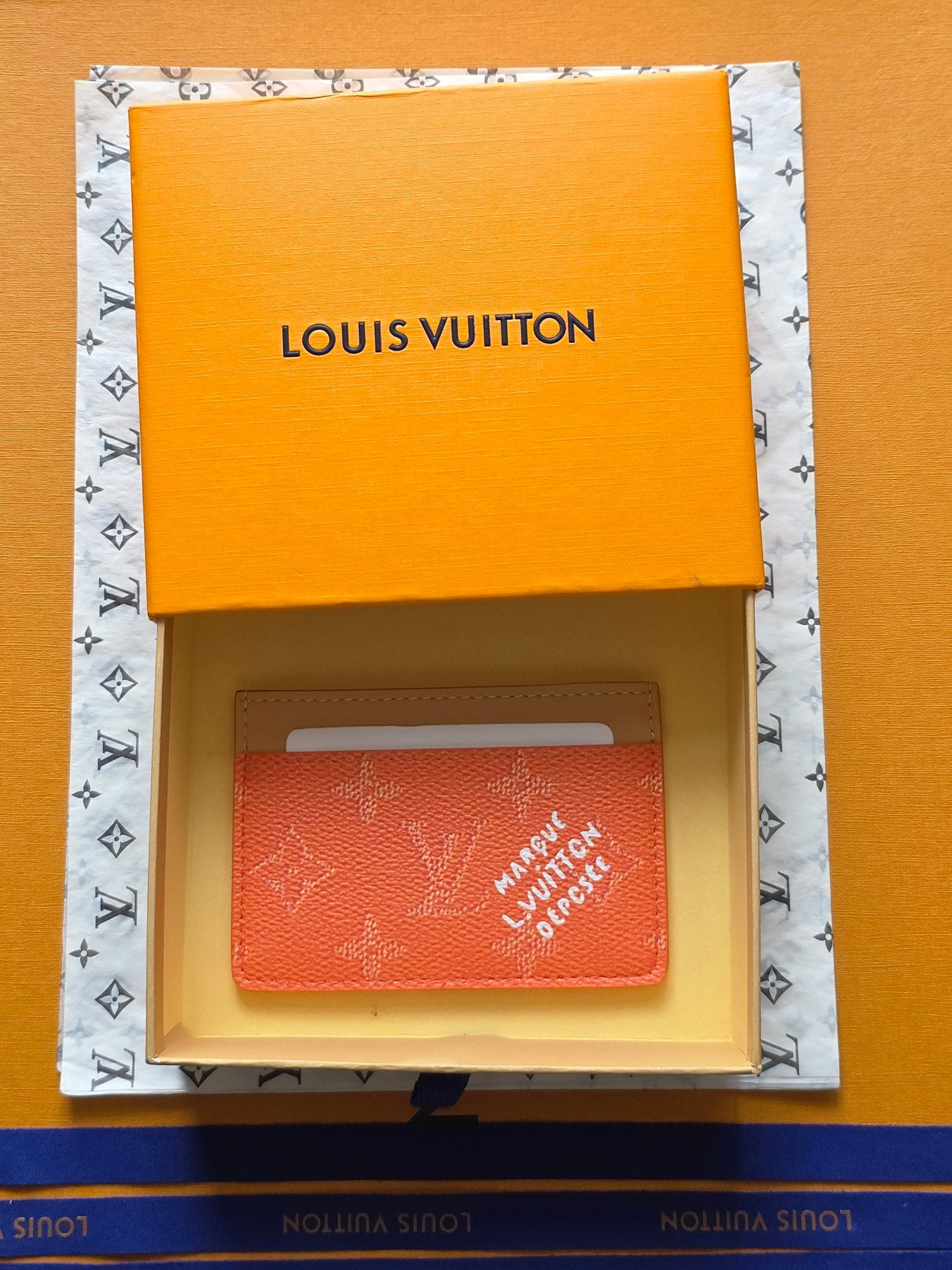 Small Louis Vuitton cardholder in coral orange, shown inside an orange gift box.