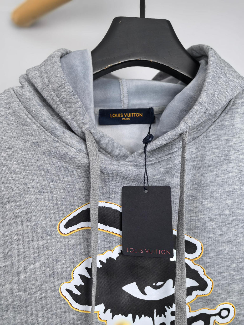 Gray kids hoodie detail with hood opening, Louis Vuitton logo tag, and drawstrings