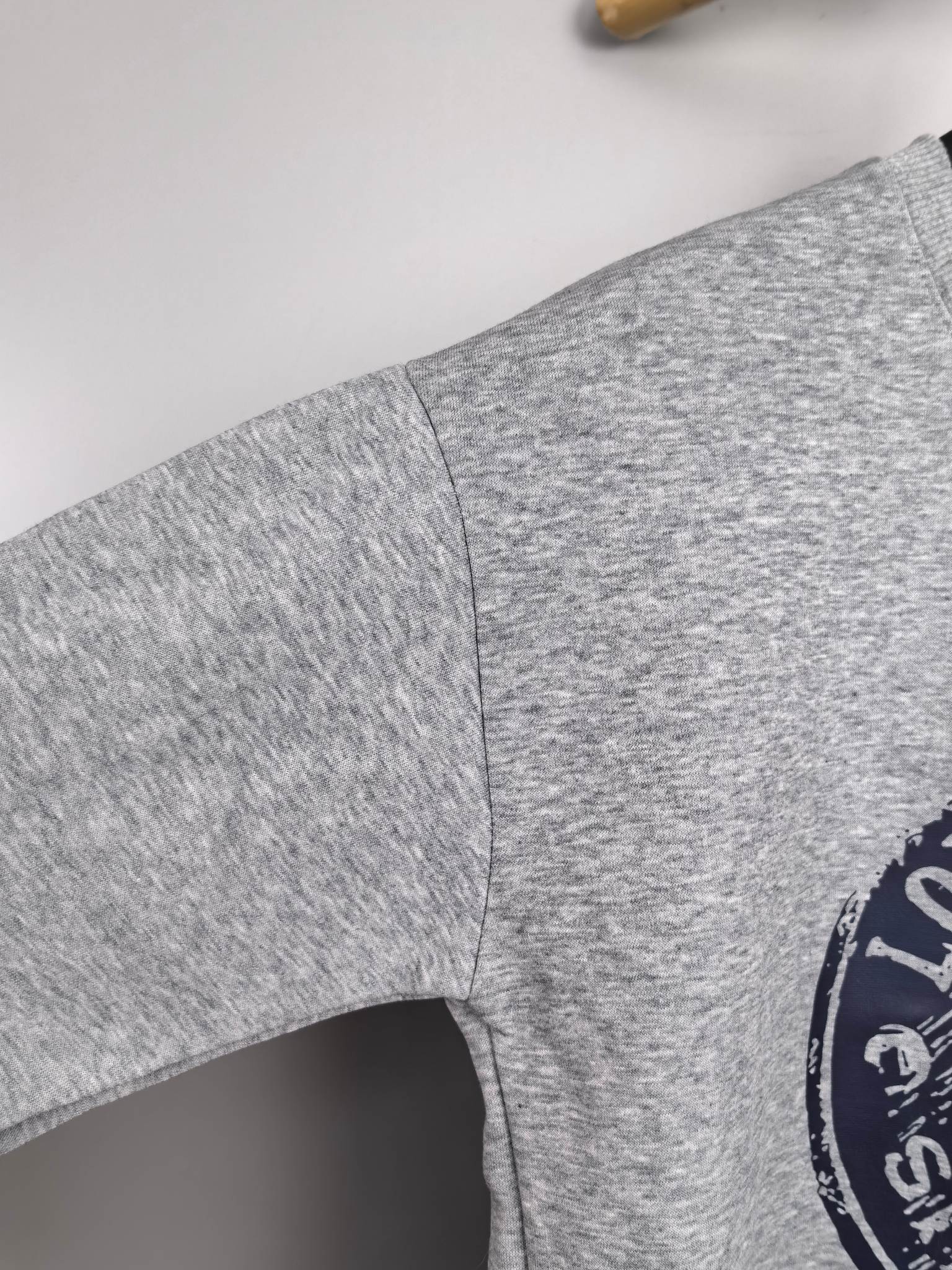 Grey sweatshirt sleeve with side seam and partial Louis Vuitton Voyage logo