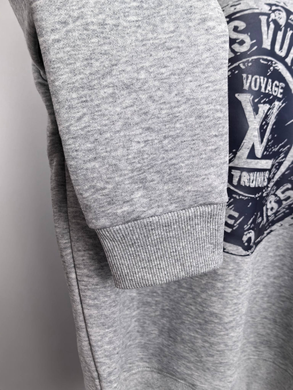 Grey sweatshirt sleeve cuff detail with partial Louis Vuitton Voyage logo