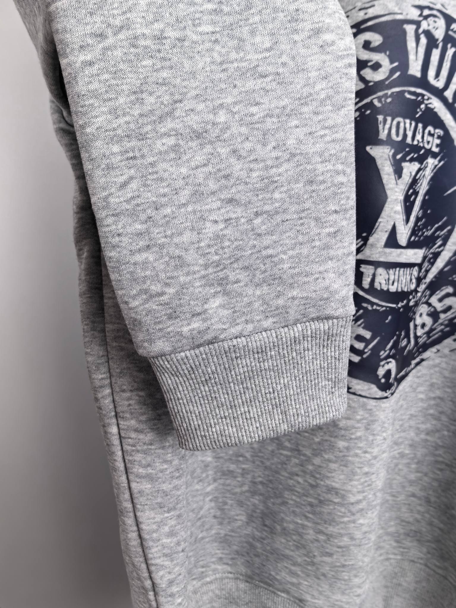 Grey sweatshirt sleeve cuff detail with partial Louis Vuitton Voyage logo
