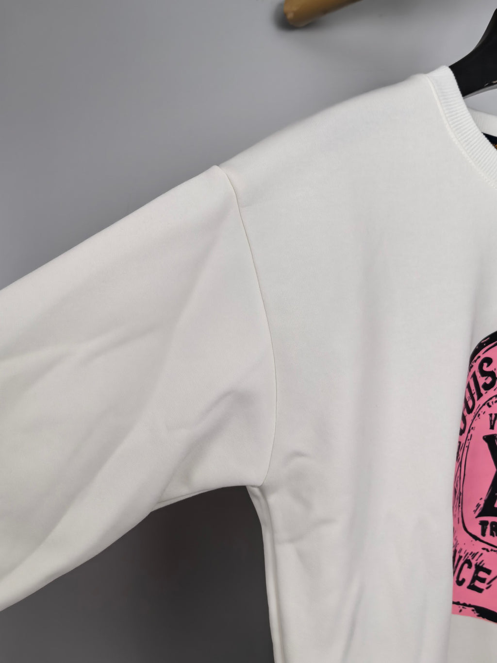 White long-sleeve sweatshirt sleeve with partial pink logo print