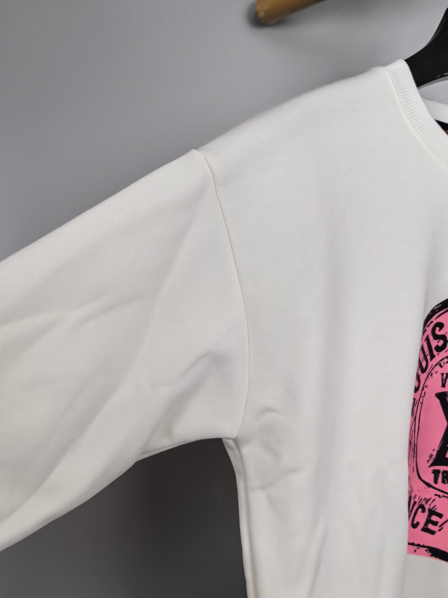 White long-sleeve sweatshirt sleeve with partial pink logo print