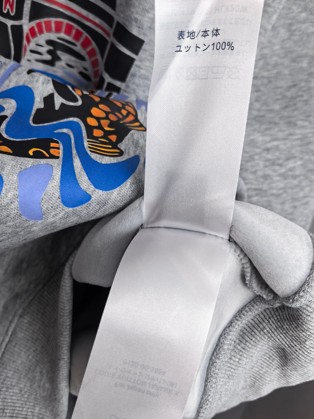 Grey sweatshirt fabric with white care tag showing unit and 100% content