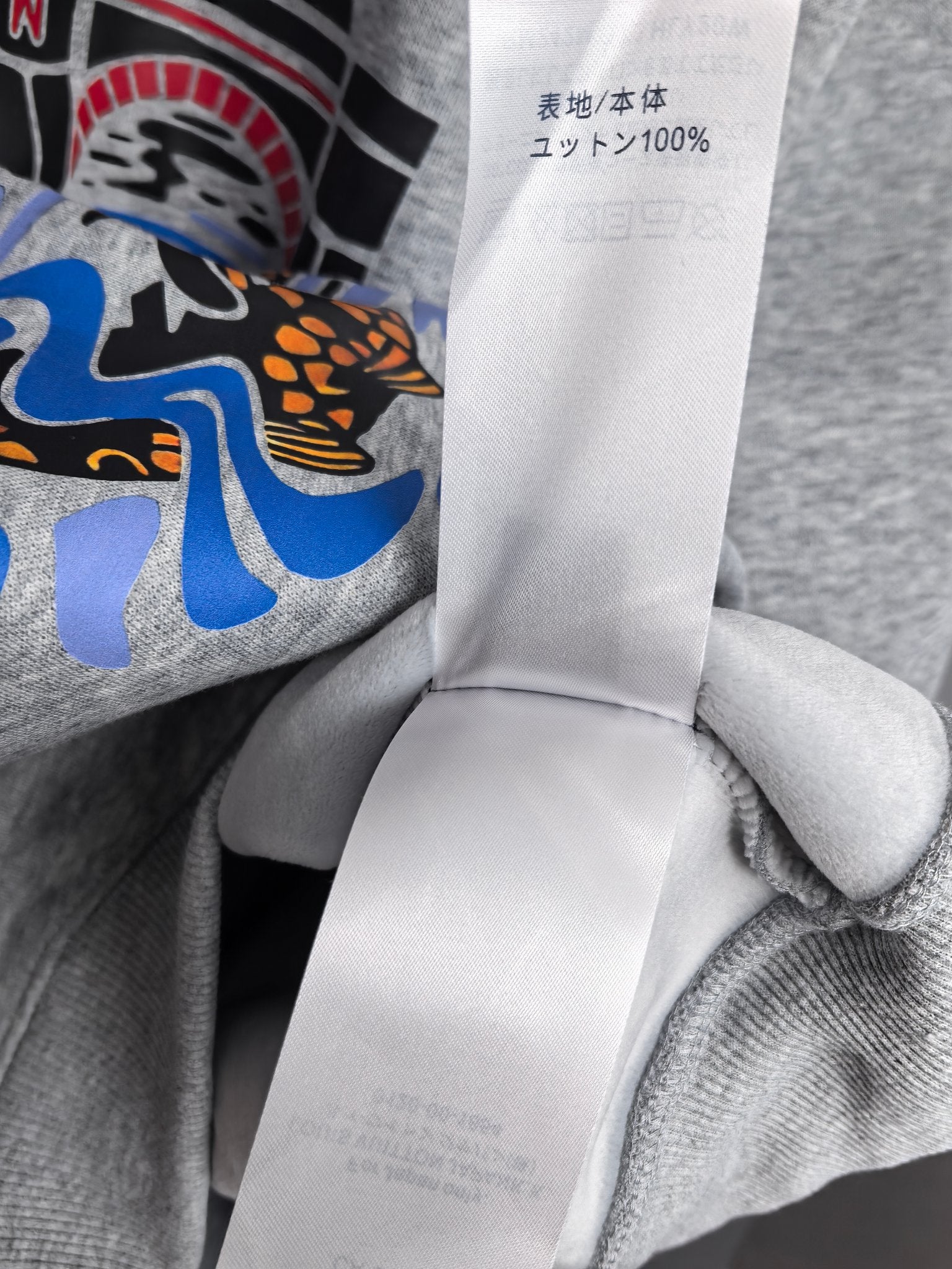 Grey sweatshirt fabric with white care tag showing unit and 100% content