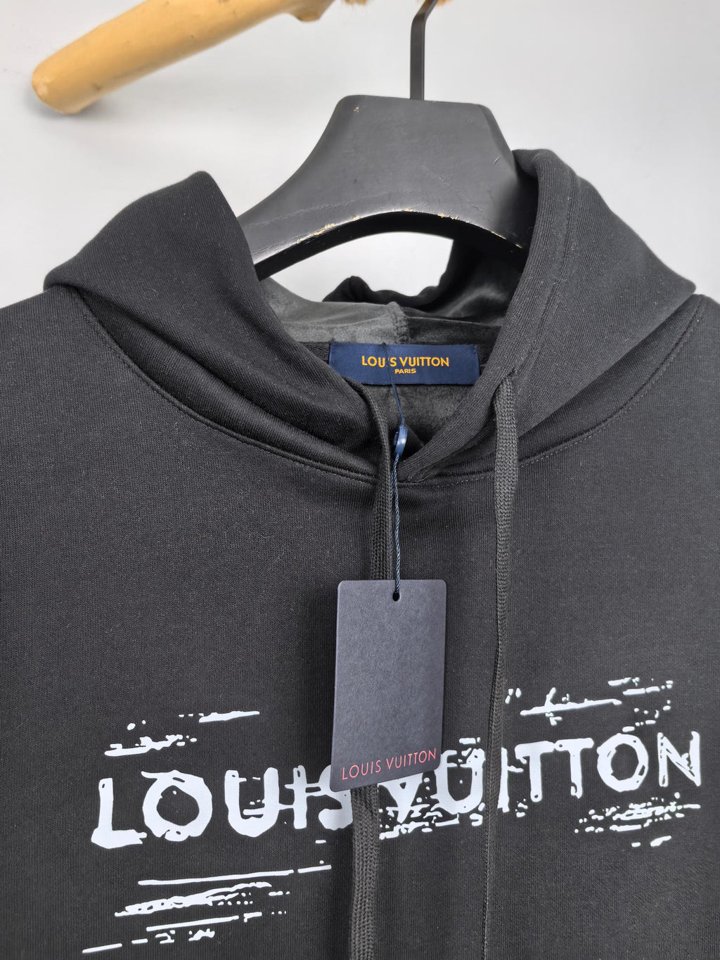 Black hoodie neckline with drawstrings and Louis Vuitton logo print, hanging tag.