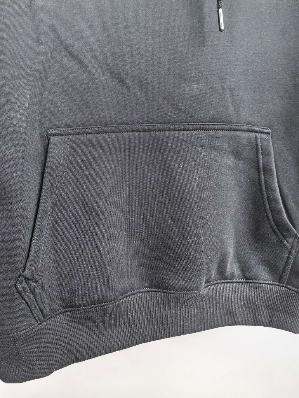 Black hoodie front pouch pocket with stitched edges and ribbed hem.