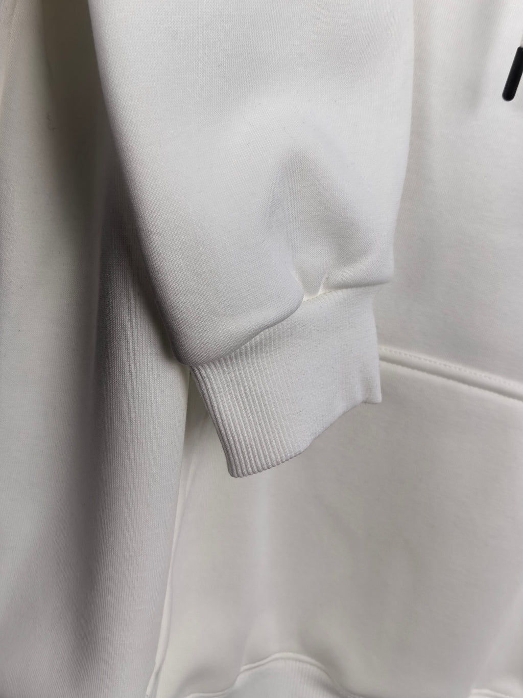 White hoodie hem and ribbed cuff detail, front pocket panel visible.