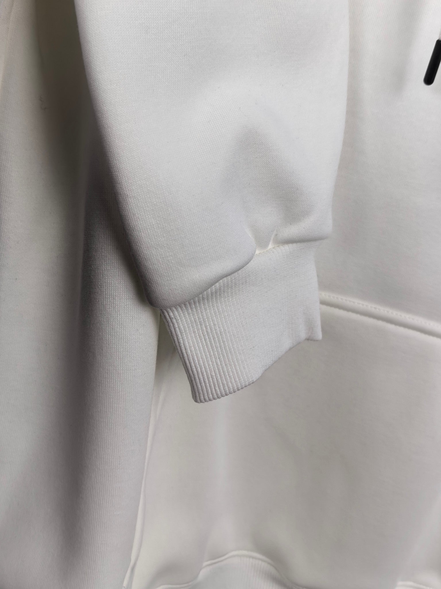White hoodie hem and ribbed cuff detail, front pocket panel visible.