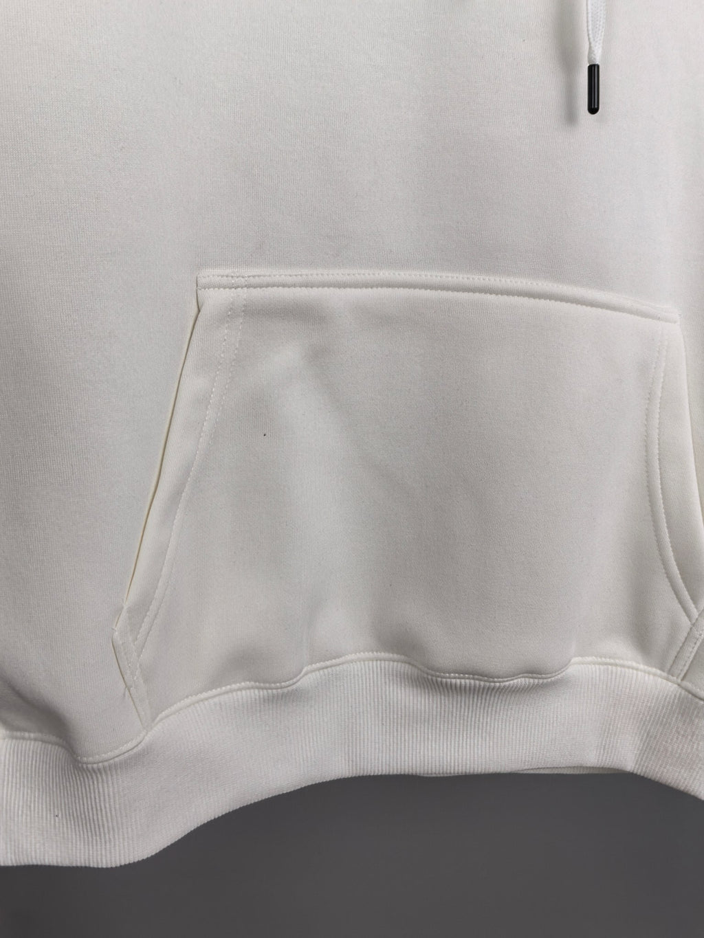 White hoodie front pocket and waistband hem detail.