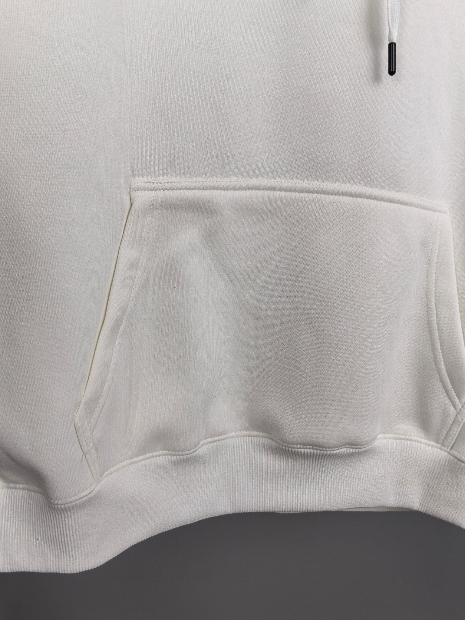 White hoodie front pocket and waistband hem detail.