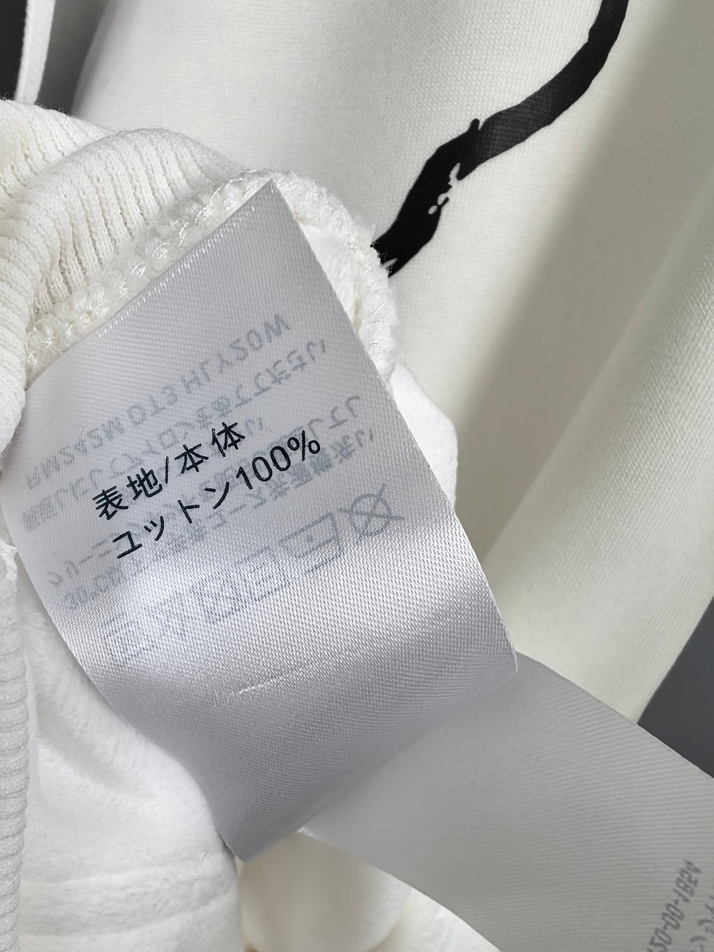 White hoodie fabric care tag inside collar with 100% content and washing marks