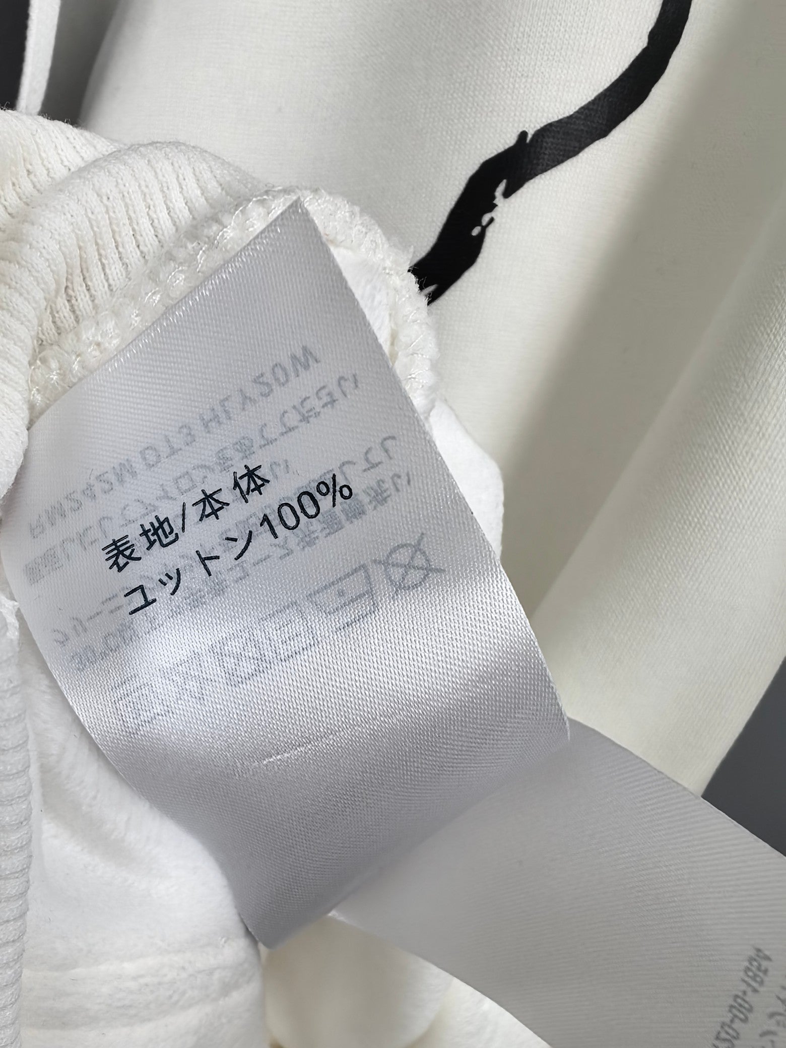 White hoodie fabric care tag inside collar with 100% content and washing marks