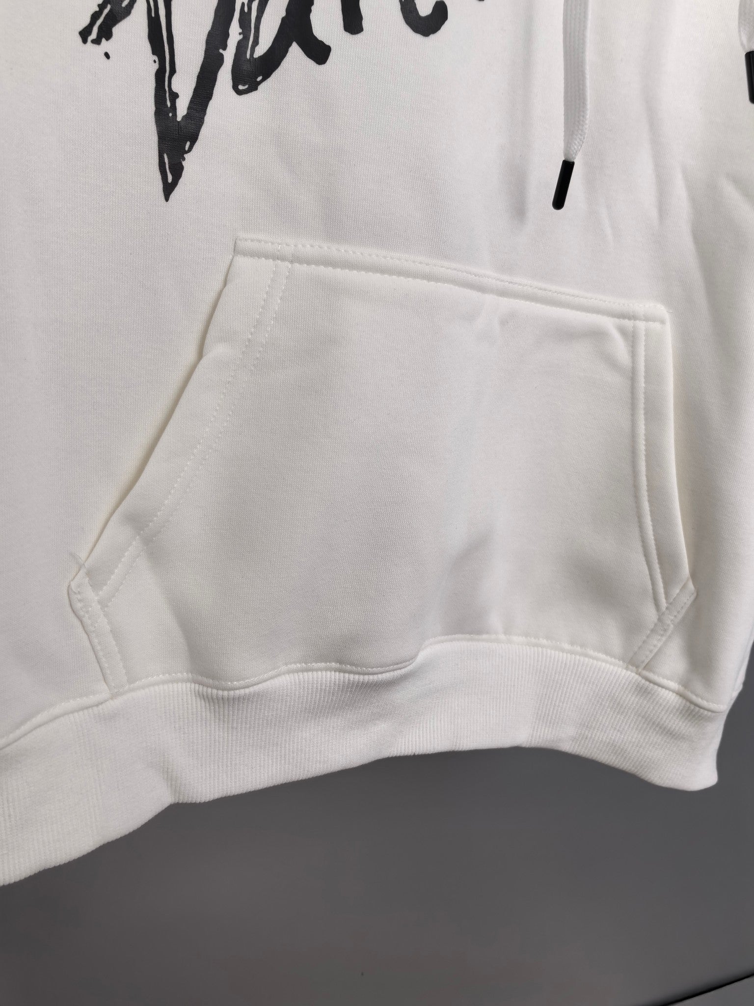 White hoodie front kangaroo pocket with ribbed hem and black graphic above