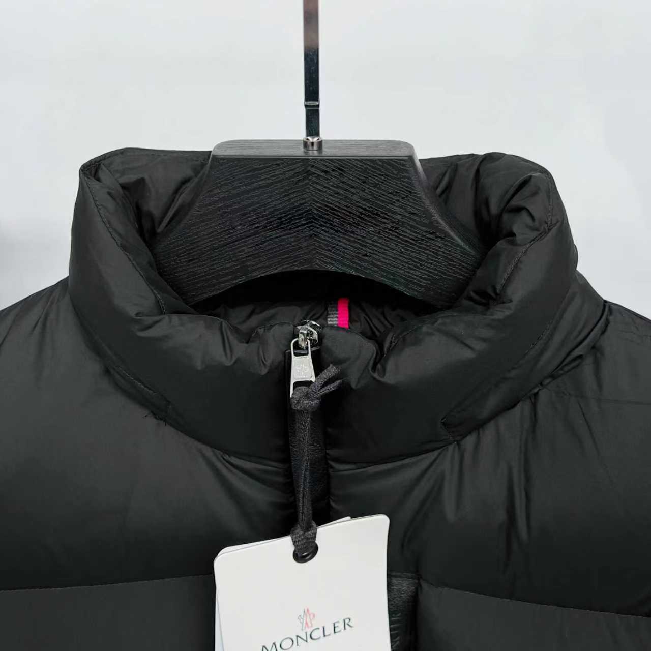 Black puffer jacket collar with half-zip front and Moncler logo hang tag