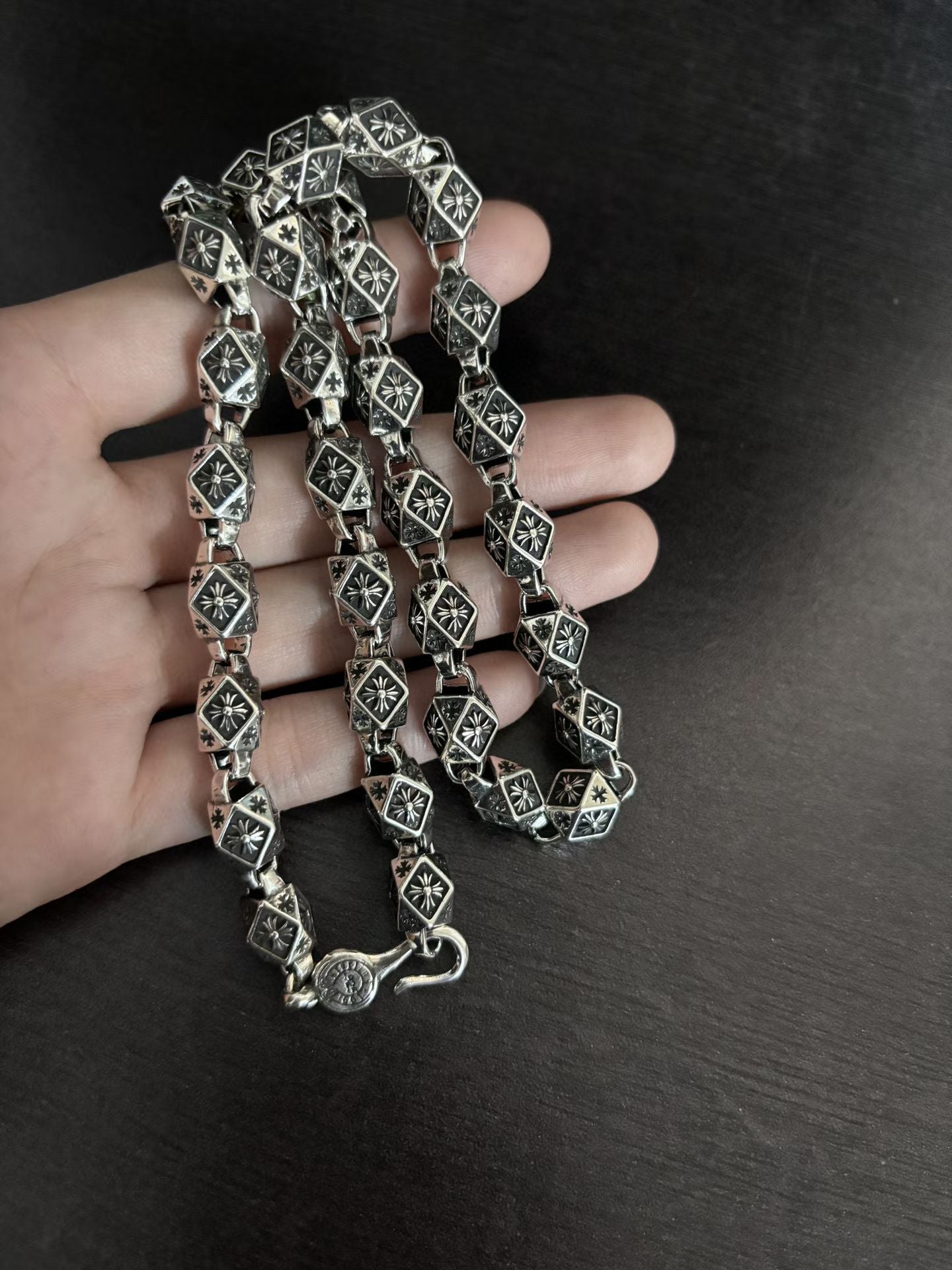 Star-motif square-link chain necklace held in hand, silver-tone with dark accents