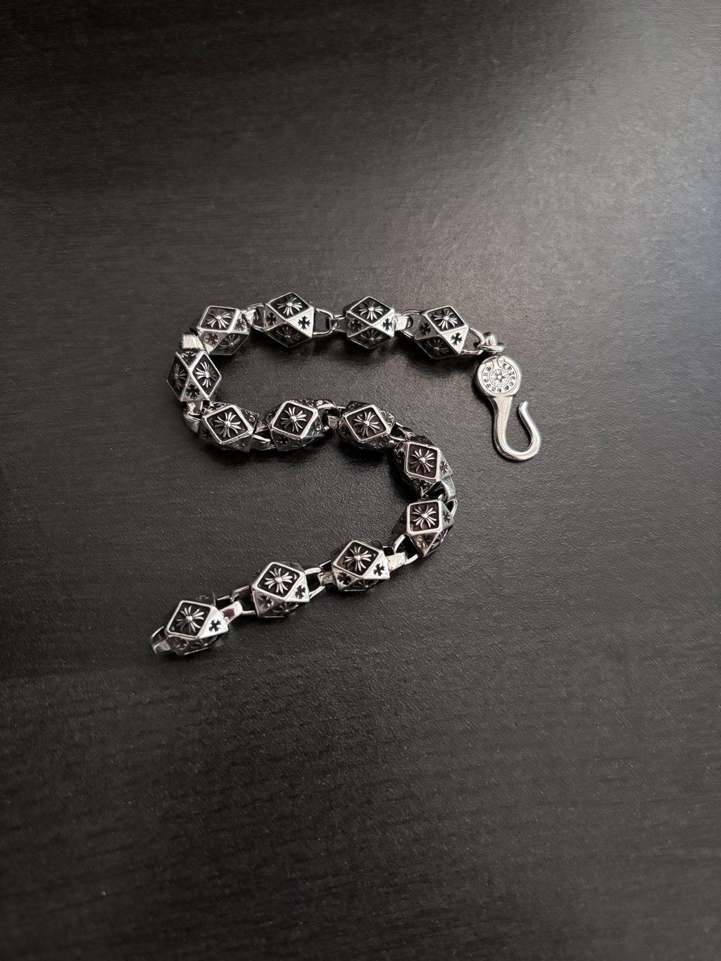 Chrome bracelet with black patterned square links and round clasp charm, open side view.