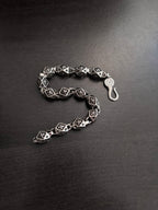 Chrome bracelet with black patterned square links and round clasp charm, open side view.