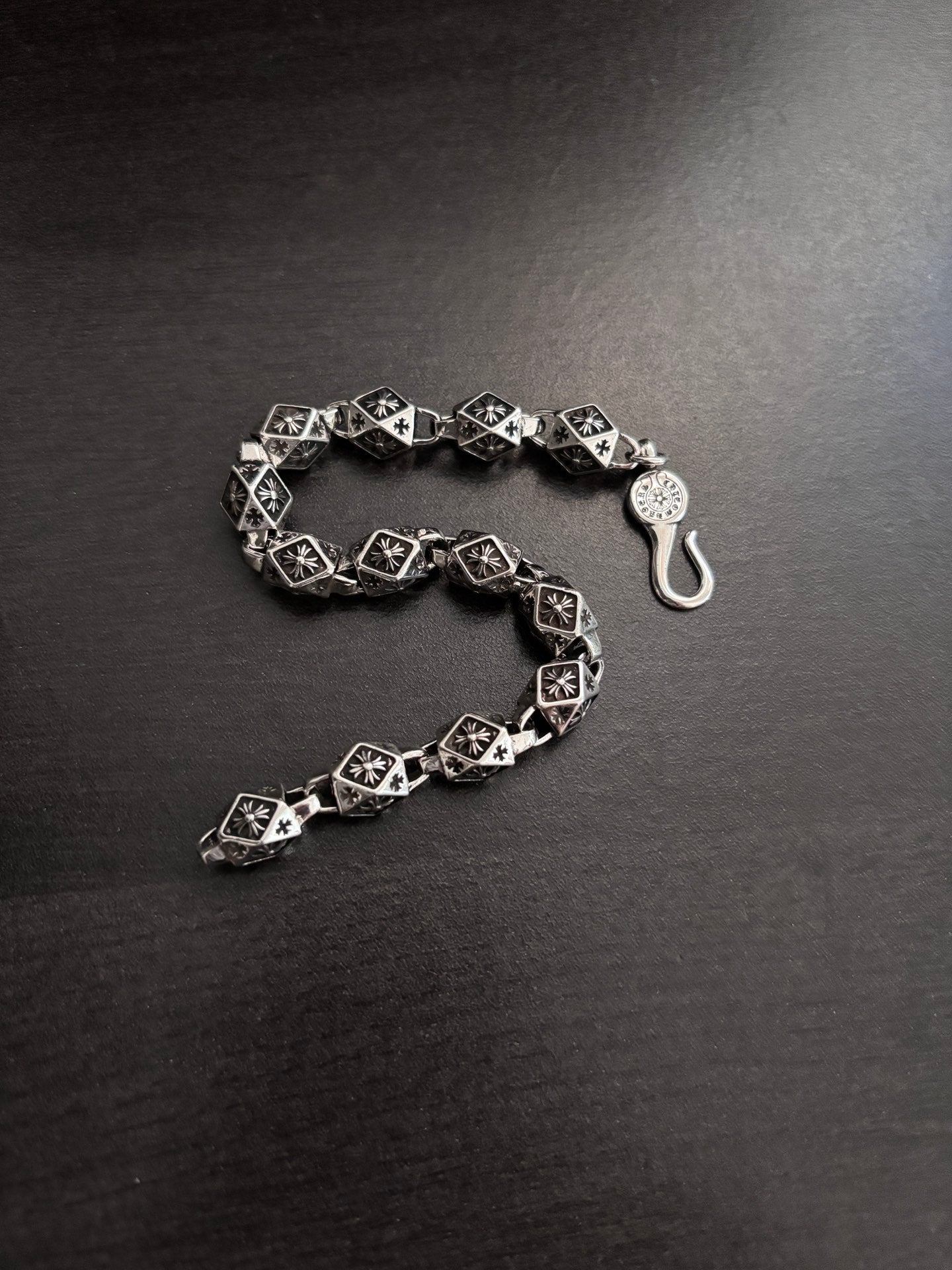 Chrome bracelet with black patterned square links and round clasp charm, open side view.