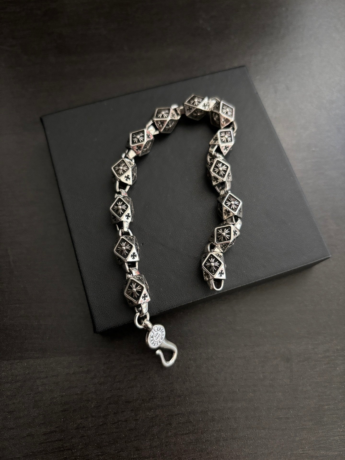 Chrome bracelet with black square links, round clasp charm, and hook closure.