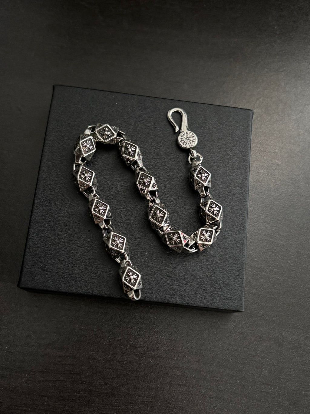 Chrome bracelet shown on a dark box, black square links with silver-tone round charm.