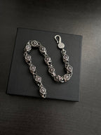 Chrome bracelet shown on a dark box, black square links with silver-tone round charm.