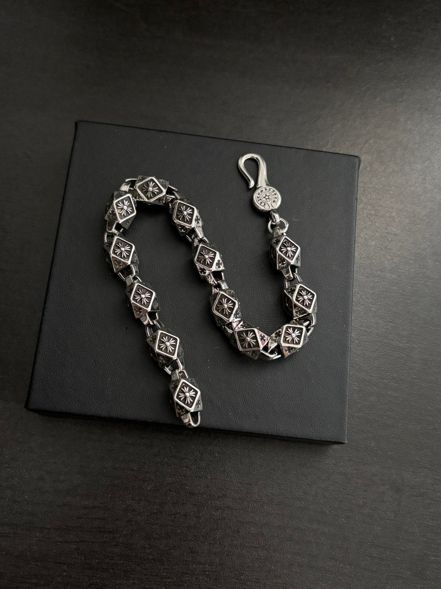 Chrome bracelet shown on a dark box, black square links with silver-tone round charm.