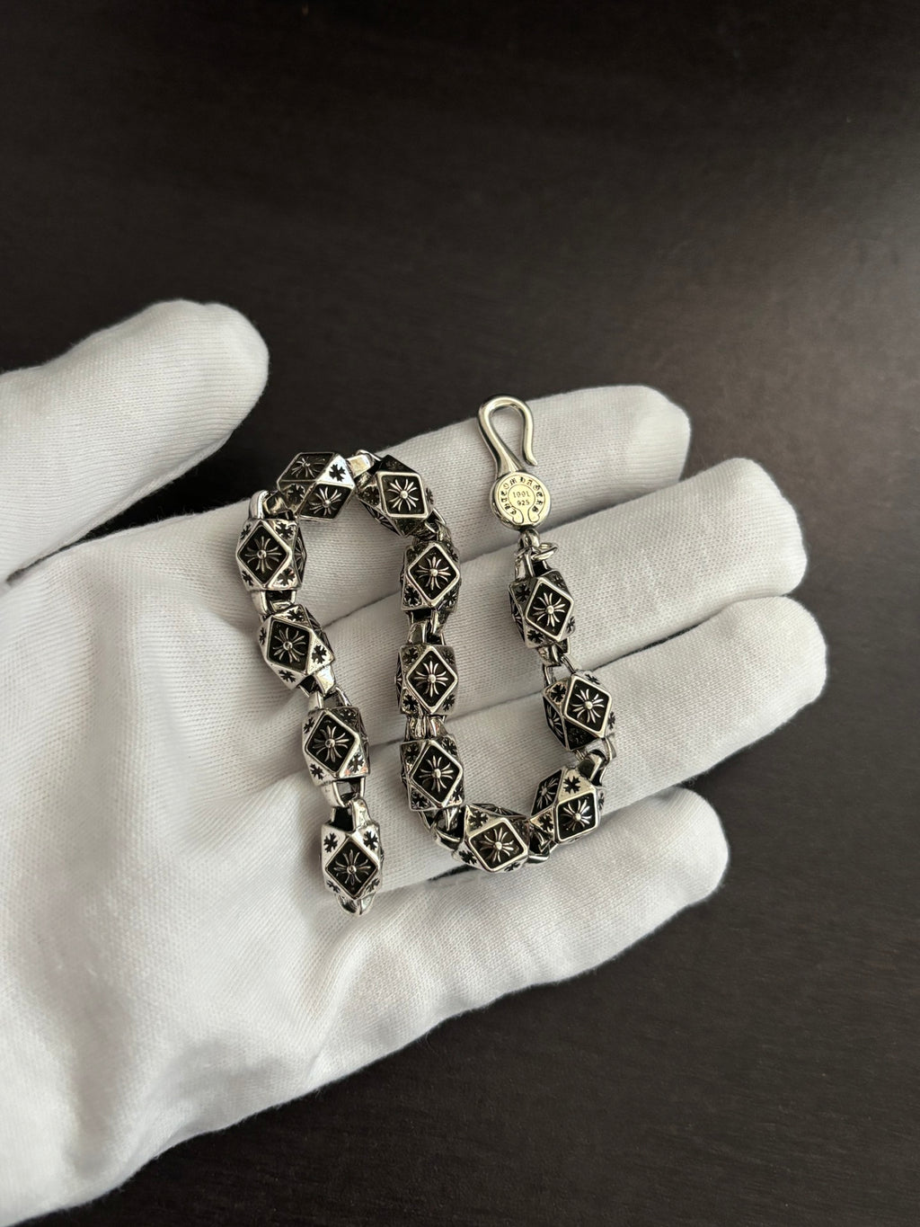 Chrome bracelet on a gloved hand, black square links with silver-tone round charm.