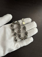 Chrome bracelet on a gloved hand, black square links with silver-tone round charm.