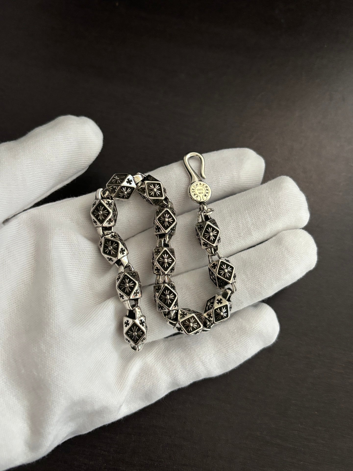 Chrome bracelet on a gloved hand, black square links with silver-tone round charm.