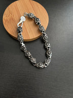 Chrome bracelet with black square links and round clasp charm, silver-tone metal.