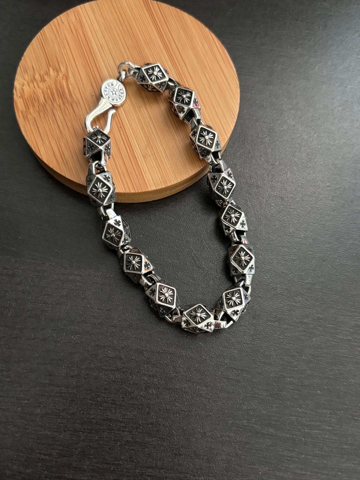 Chrome bracelet with black square links and round clasp charm, silver-tone metal.