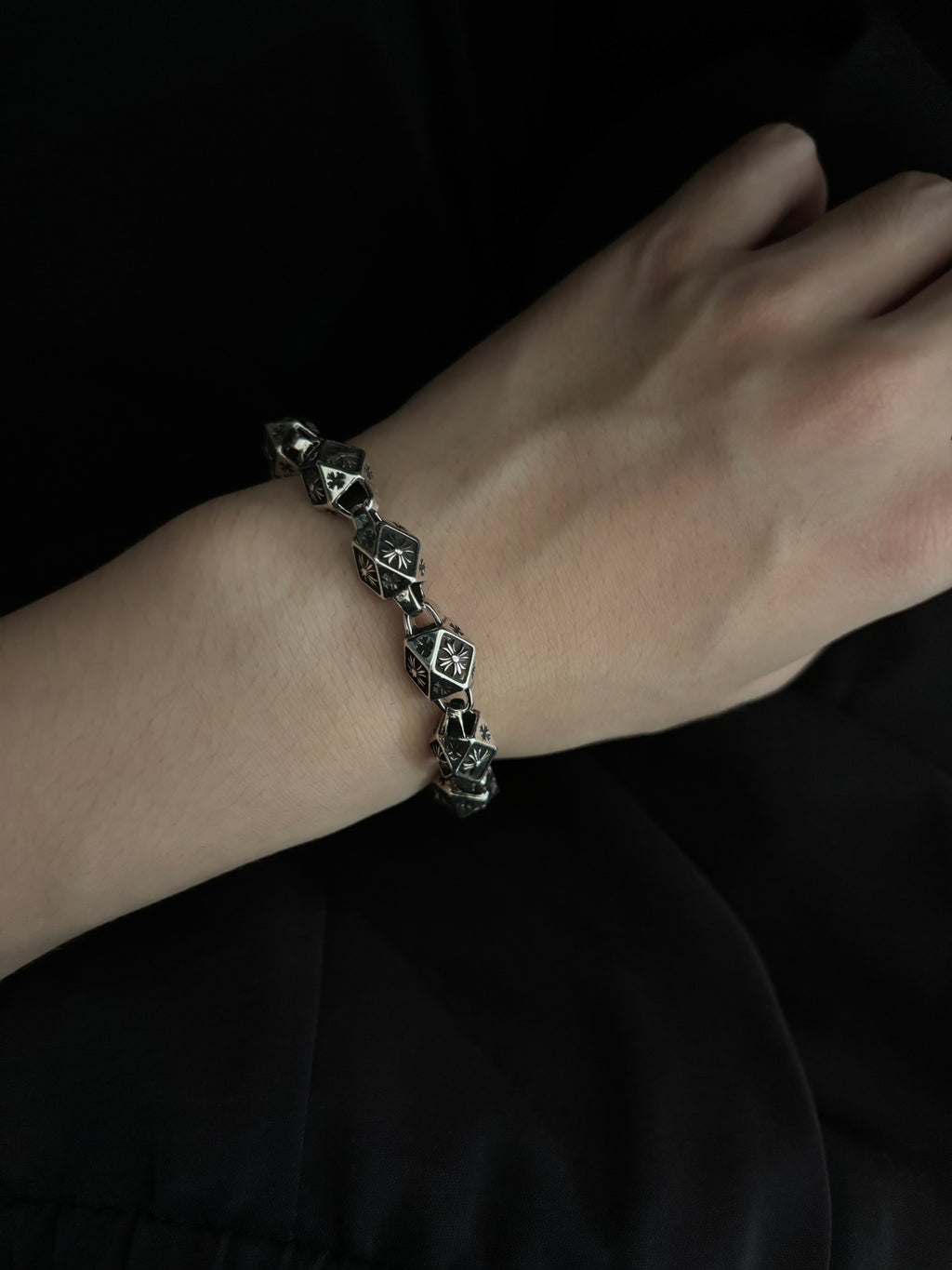 Chrome bracelet on wrist, black square links with silver-tone metal and round charm.