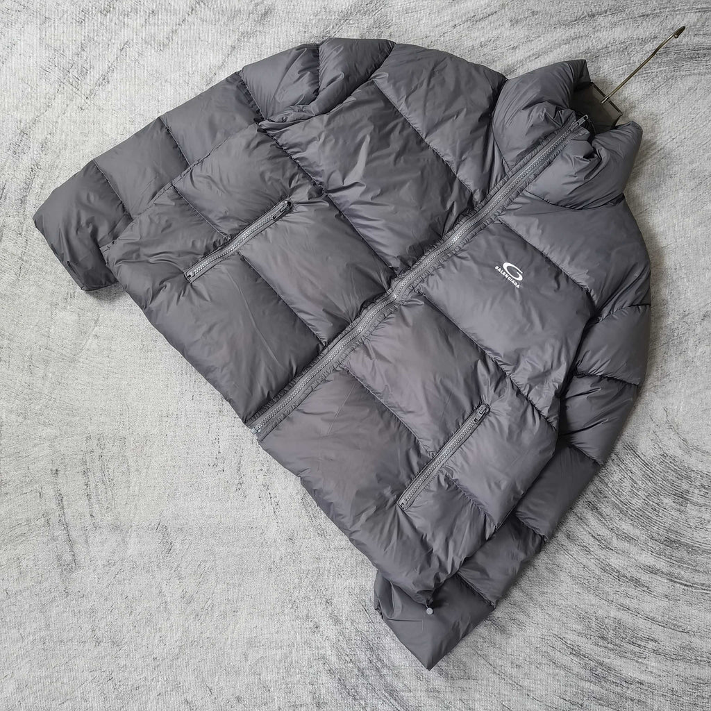Gray Balenciaga puffer jacket laid out, angled view with zip front and chest logo.