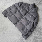 Gray Balenciaga puffer jacket laid out, angled view with zip front and chest logo.