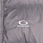Balenciaga logo patch on gray puffer jacket chest panel, white oval icon and text.