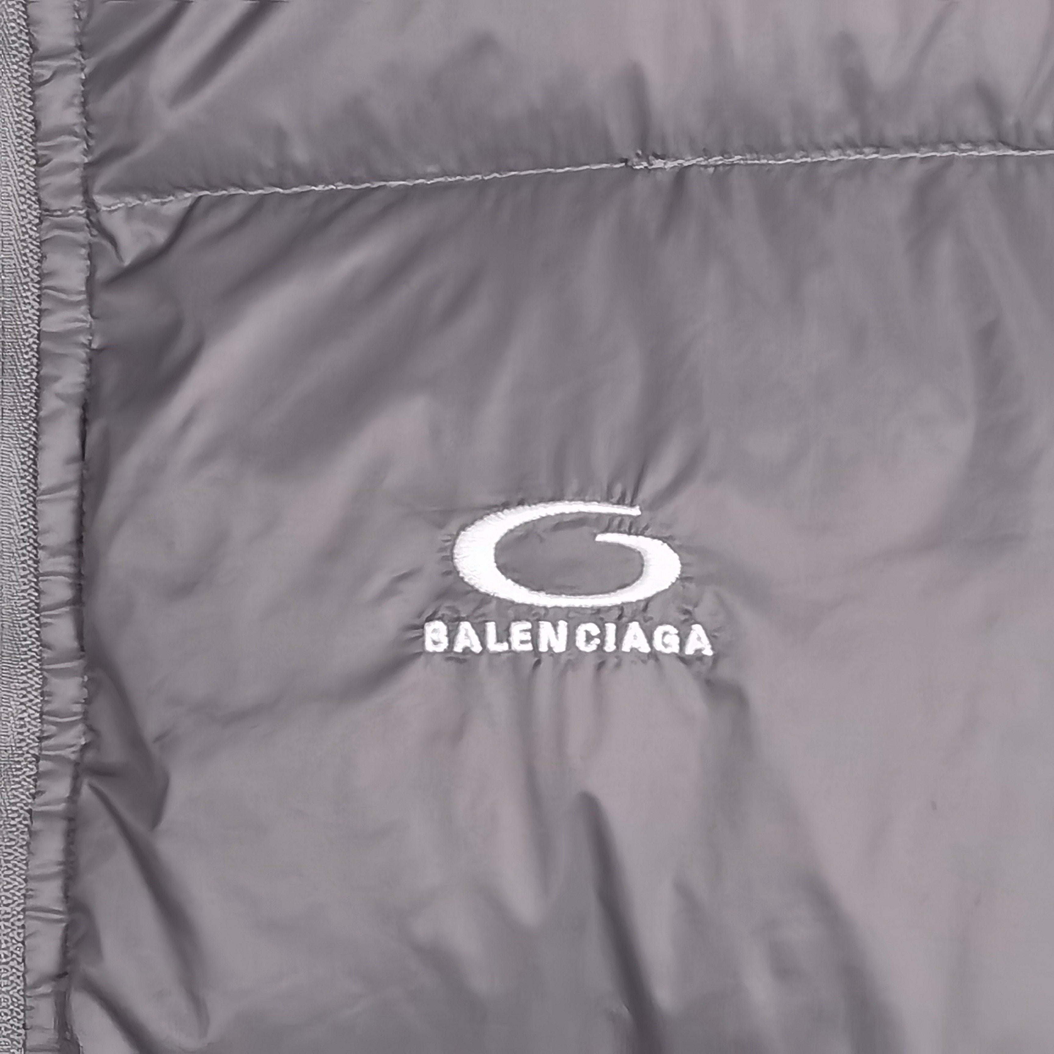 Balenciaga logo patch on gray puffer jacket chest panel, white oval icon and text.