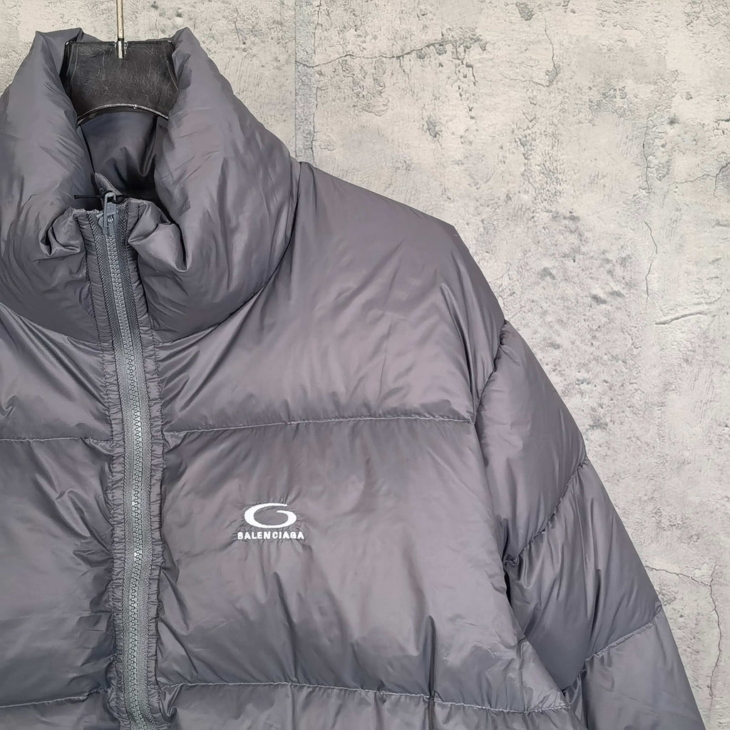 Gray Balenciaga puffer jacket front close-up with high collar, zipper placket, logo.