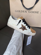 White low-top sneakers with black laces, gold trim, and leopard print side panel