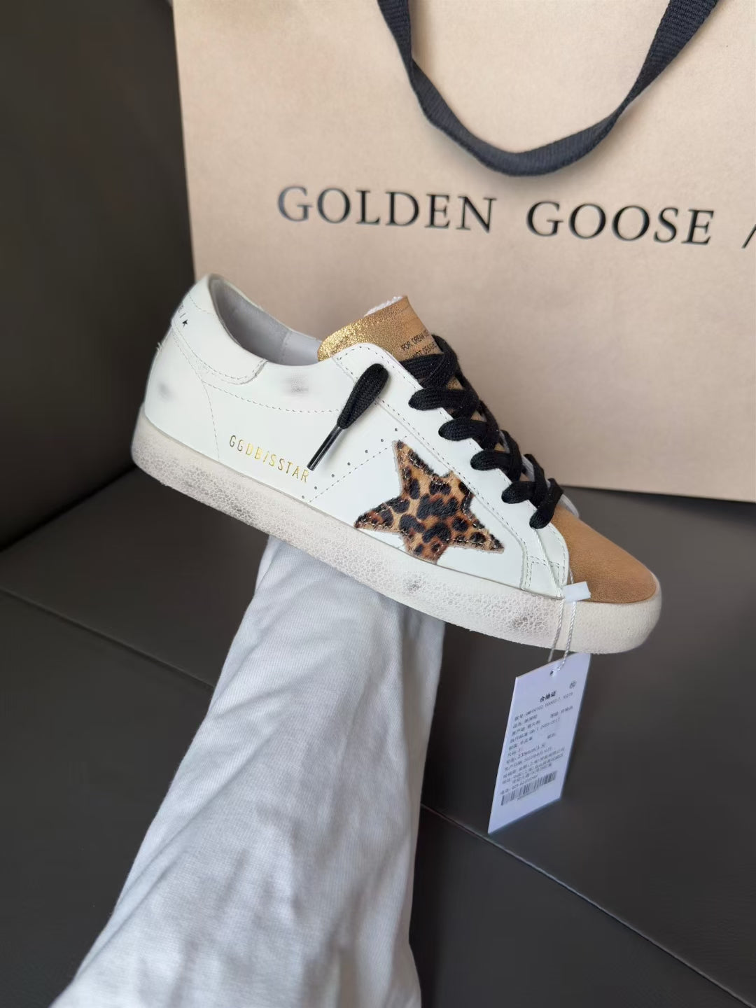 White low-top sneakers with black laces, gold trim, and leopard print side panel