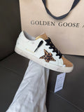 White leather sneaker with black laces, leopard star patch, and gold toe cap.