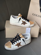 White leather sneakers with black laces, gold panels, and leopard print star accent