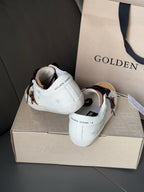 White leather sneakers from the back with black laces and gold toe caps.