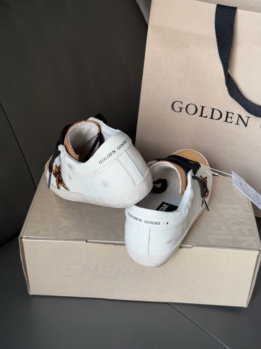 White leather sneakers from the back with black laces and gold toe caps.